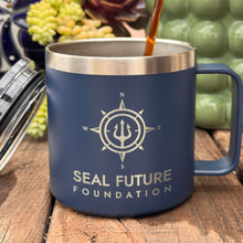 Load image into Gallery viewer, Blue mug with 'SEAL Future Foundation' logo being filled with a liquid, placed on a wooden surface with plants in the background.